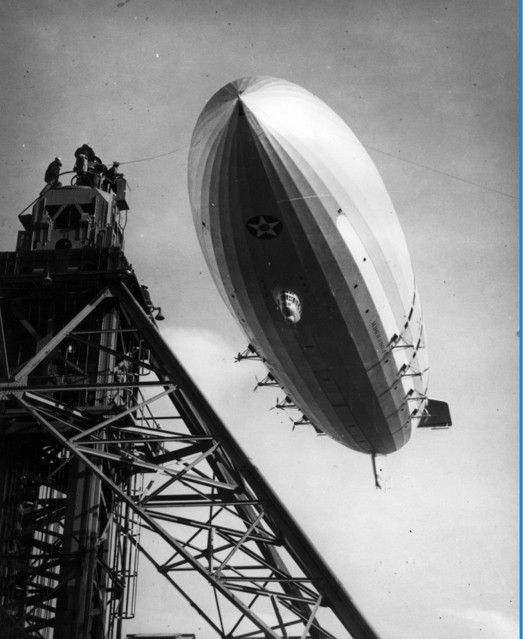 An old photo of a large blimp flying over a building.